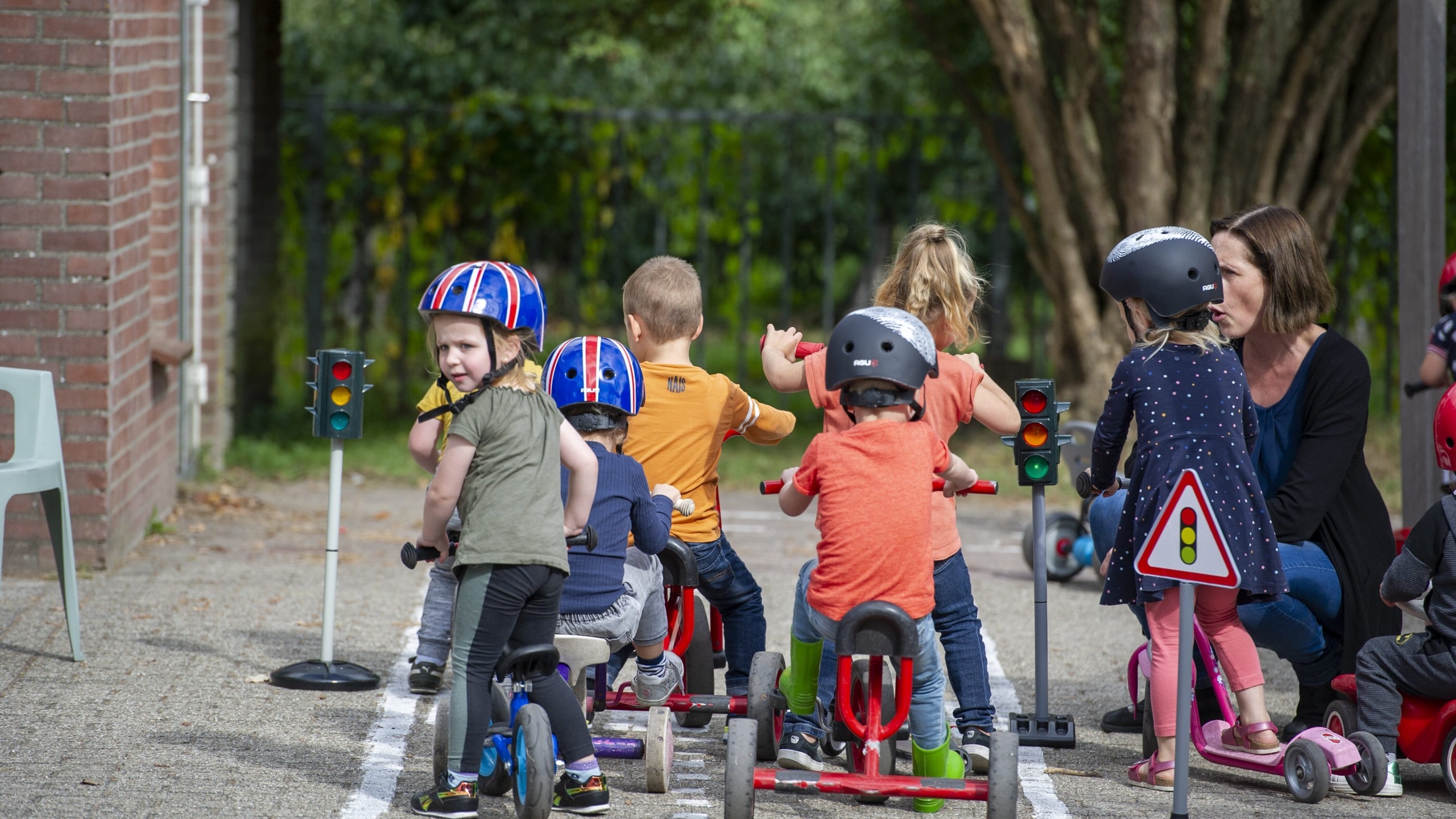Peuters op stepfietsjes met een helm op het schoolplein dat is ingericht als verkeersplein