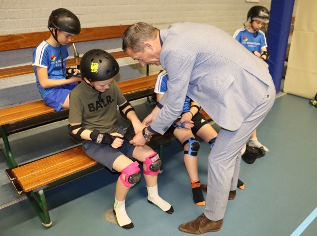 Wethouder helpt leerling bij aantrekken skates