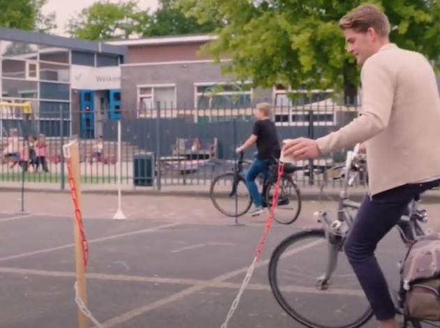 Afbeelding van kettingproef op de fiets, waarbij een fietser een beker aan een ketting op een paaltje probeert te zetten