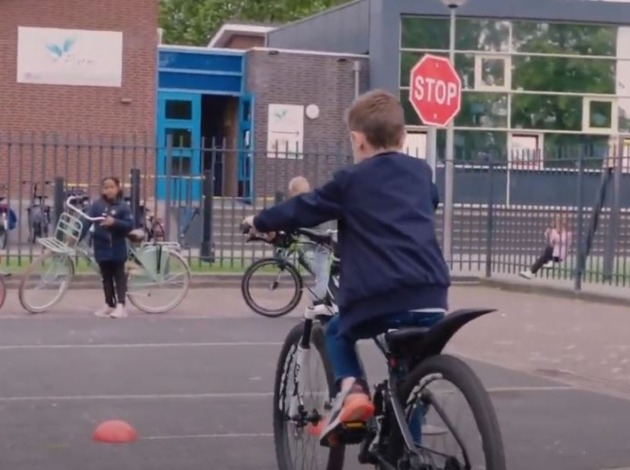 Jongen op fietsparkoers op het schoolplein fietst tussen pionnen door