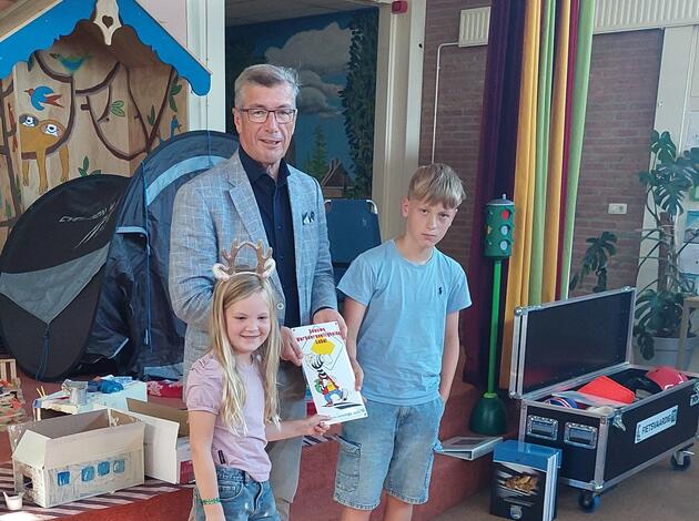 wethouder John de Jonge reikt muurbord verkeerslabel uit aan 2 leerlingen