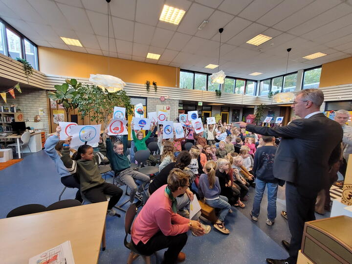 Gedeputeerde bekijkt tekening die leerlingen omhoog houden